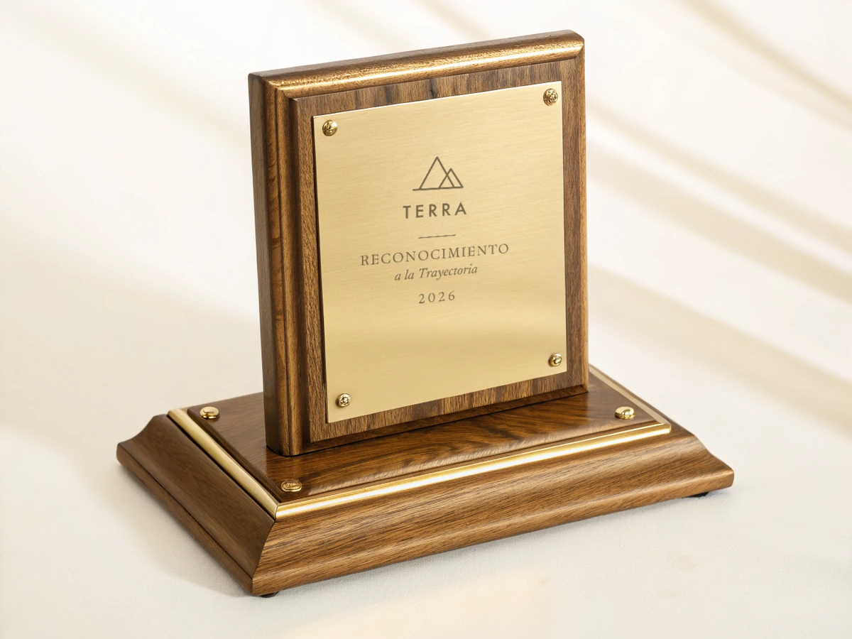 reconocimiento de escritorio con una placa de latón grabada TERRA y Reconocimiento a la Trayectoria 2026, enmarcada en nogal y montada sobre una base escalonada rematada con un filete dorado