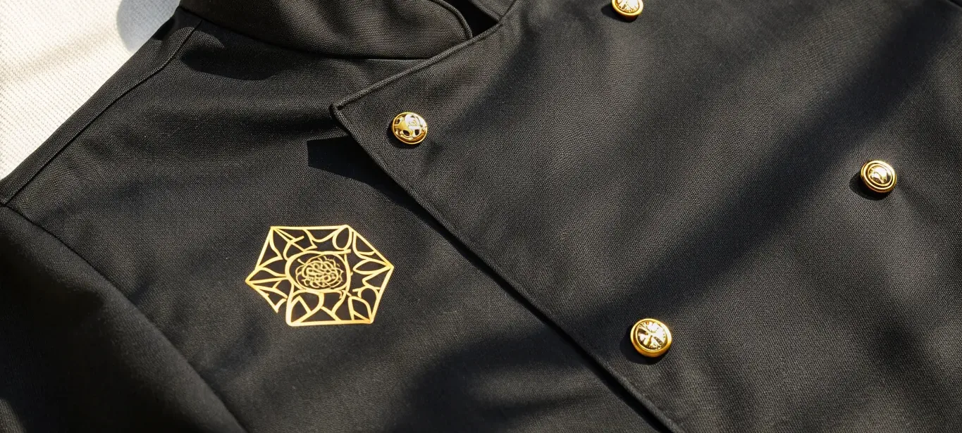 acercamiento a una chaqueta de servicio cruzada en sarga de algodón negro con luz rasante sobre el tejido, y cuatro botones dorados en domo con una roseta labrada en el centro