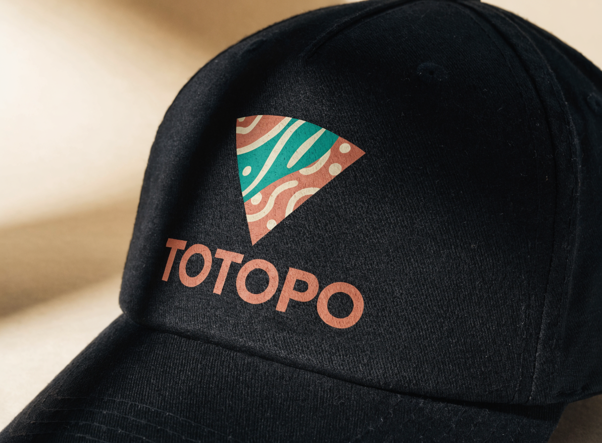 acercamiento a la copa de una gorra negra de sarga con un triángulo estampado en terracota y turquesa y la palabra TOTOPO debajo, con la tinta abierta sobre el tejido