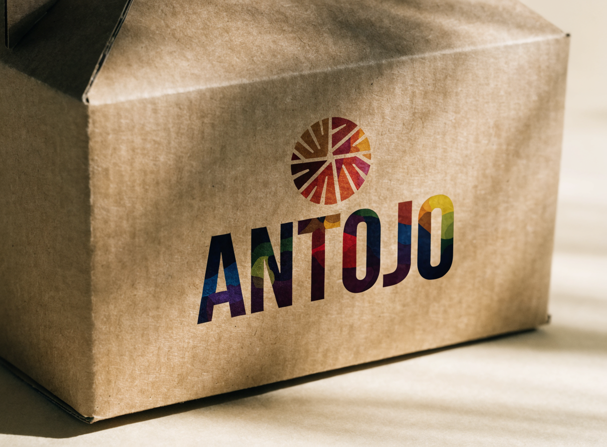 caja gable de cartón kraft en primer plano con la marca ANTOJO y un sol de colores impresos a todo color sobre la fibra del papel