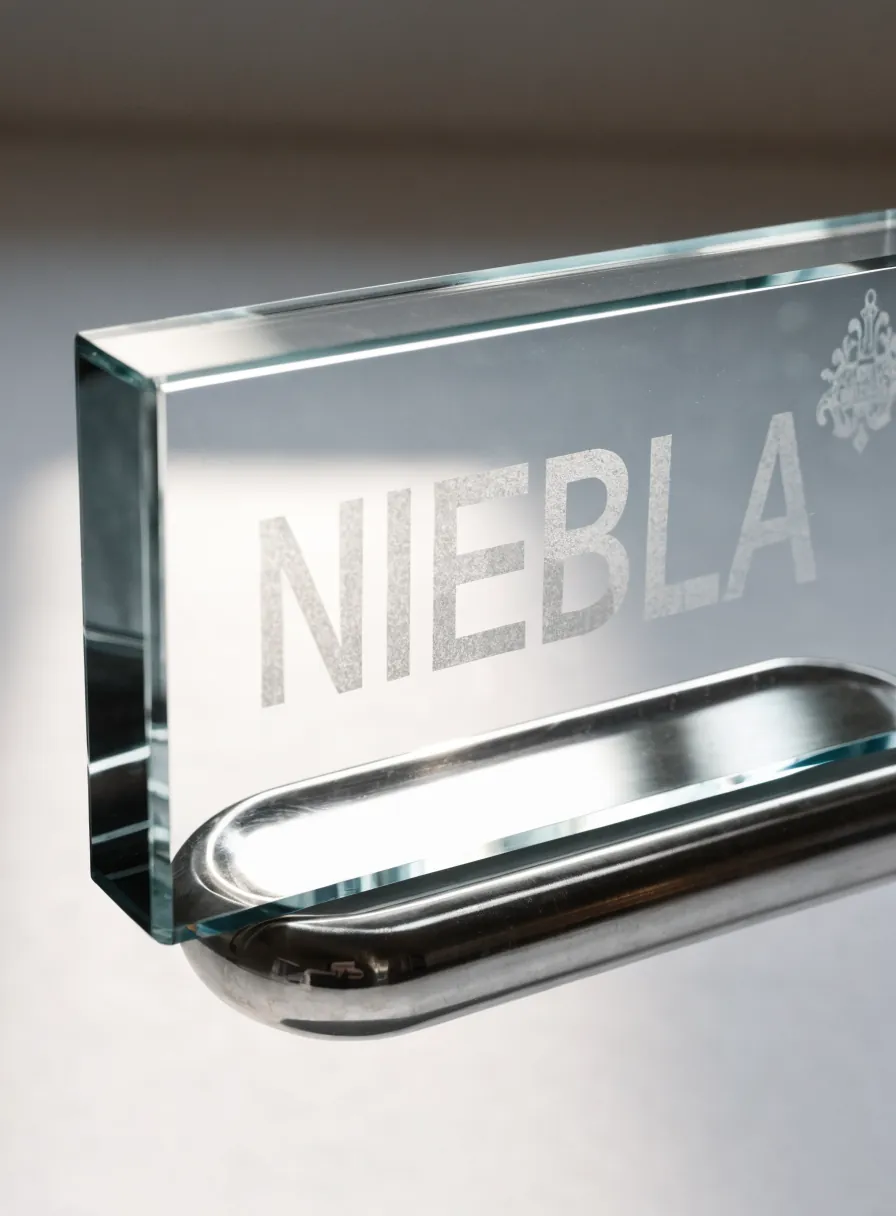 placa de cristal biselado con el nombre Niebla grabado al arenado en mate y un escudo, montada sobre una base de metal cromado