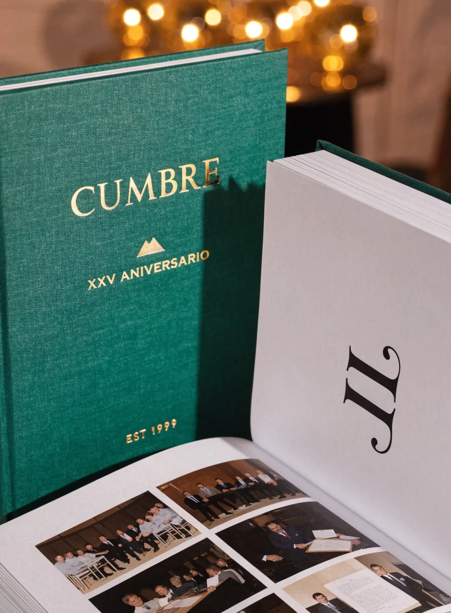 libro conmemorativo forrado en tela verde con la marca Cumbre y XXV Aniversario en foil oro, junto a un libro abierto con fotografías de la gala