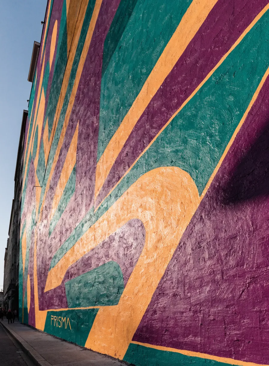 mural exterior pintado a mano con un abanico geométrico en teal, morado y naranja y el nombre de la marca ficticia PRISMA, sobre la fachada de un edificio a pie de calle