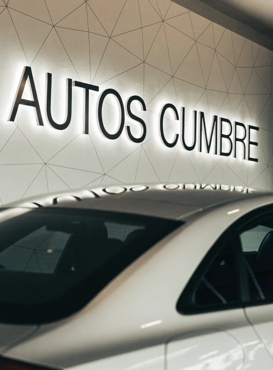 letras dimensionales retroiluminadas Autos Cumbre en el muro del showroom, con un auto blanco debajo