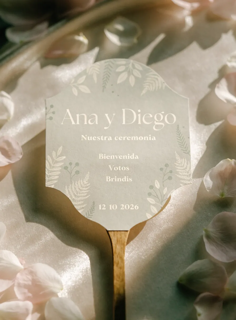 abanico de ceremonia con mango de madera y tarjeta verde salvia que dice Ana y Diego, nuestra ceremonia, bienvenida, votos, brindis y la fecha, entre pétalos