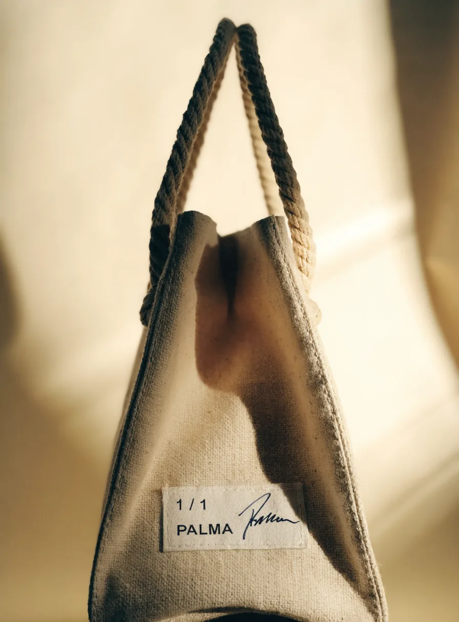 bolsa de lona de algodón natural cosida a la medida, con asas de cordón grueso y una etiqueta de tela cosida que dice uno de uno PALMA junto a la firma del taller, sobre fondo cálido