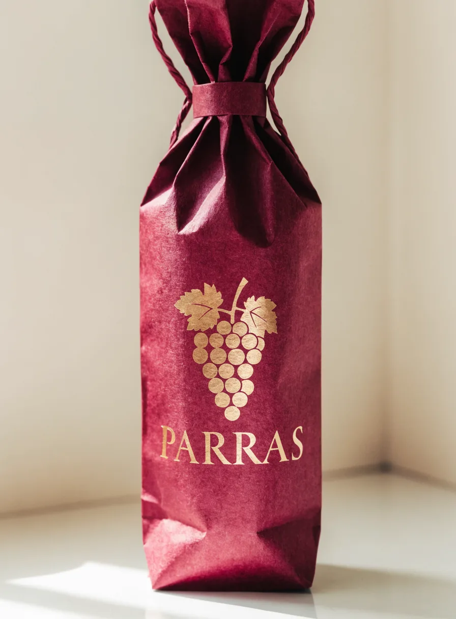 bolsa de papel para botella color vino con un cordón para cerrar y un racimo de uvas con la marca Parras en foil oro