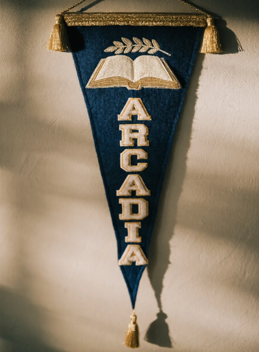 banderín de fieltro azul marino con galón y borlas doradas, el escudo del colegio con un libro abierto bajo una rama de laurel, y la palabra Arcadia bordados en aplicación de fieltro