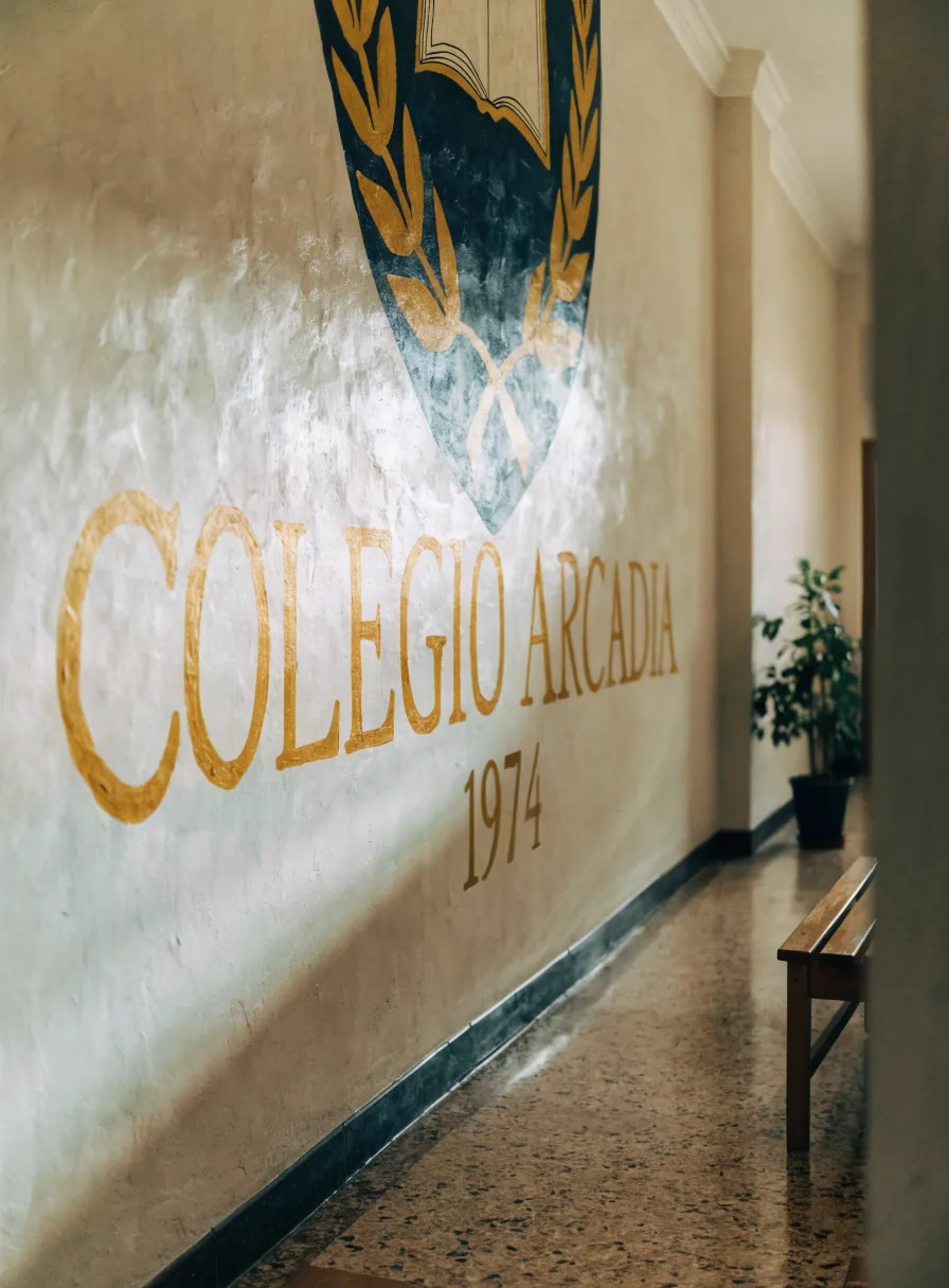 mural pintado a mano en el pasillo del campus, con el escudo del colegio sobre un escudo heráldico azul y la leyenda Colegio Arcadia 1974 en letras doradas sobre el muro