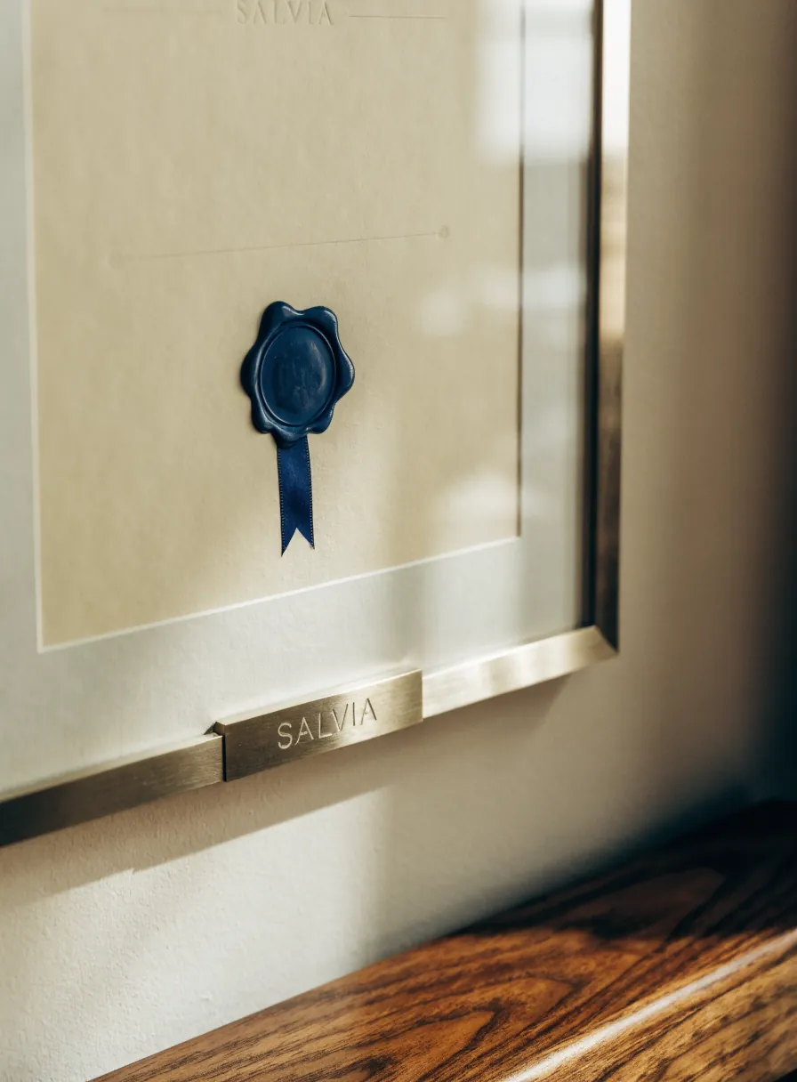 reconocimiento enmarcado en un marco de latón cepillado, con un lacre azul marino y listón sobre el papel, y una placa de latón grabada con la marca Salvia montada bajo el marco