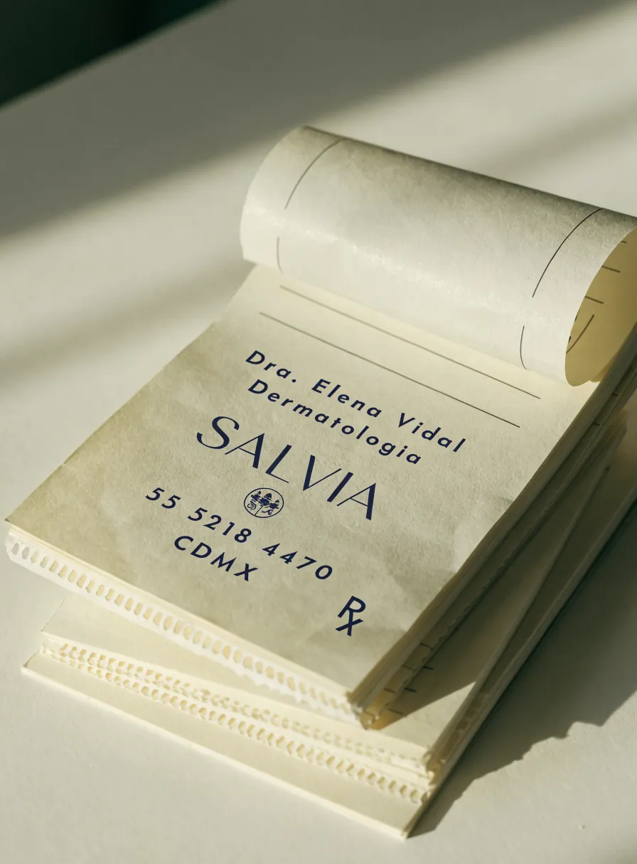 talonario de recetas médicas con las hojas impresas en azul marino con el nombre de la doctora, la marca Salvia y el símbolo de receta, sobre un escritorio claro