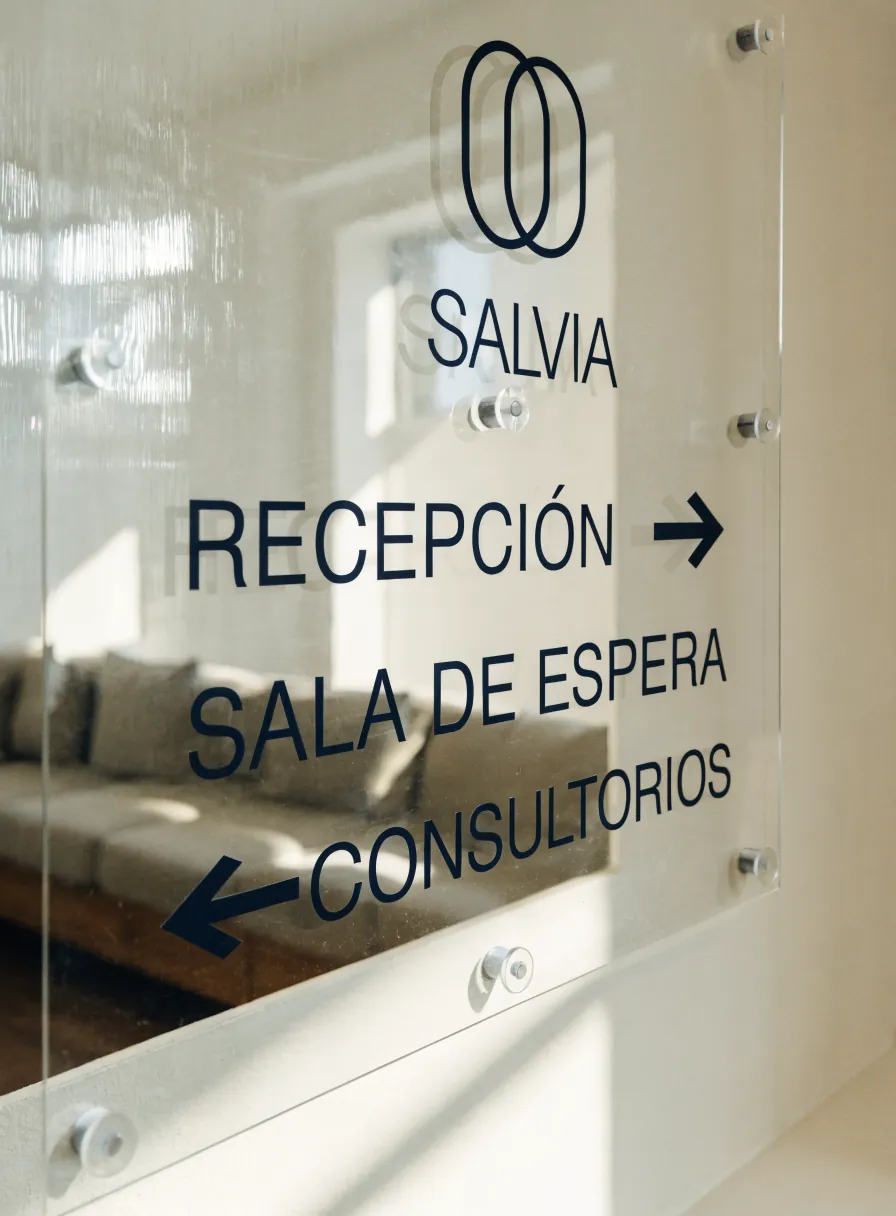 letrero de recepción en vidrio montado sobre el muro, con la marca Salvia y las direcciones a recepción, sala de espera y consultorios en azul marino