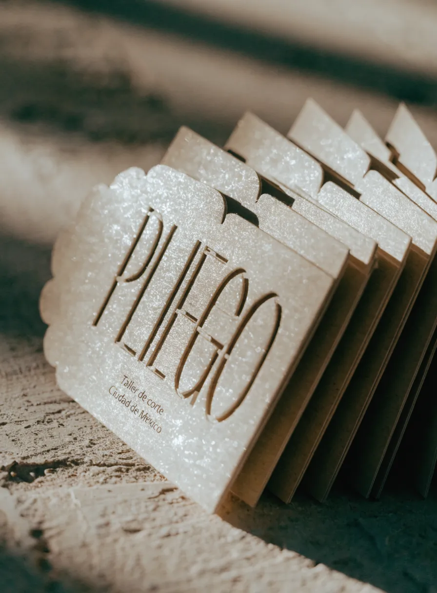 tarjetas de algodón apiladas en abanico con la palabra PLIEGO calada a través del papel y el borde festoneado con troquel, bajo luz cálida