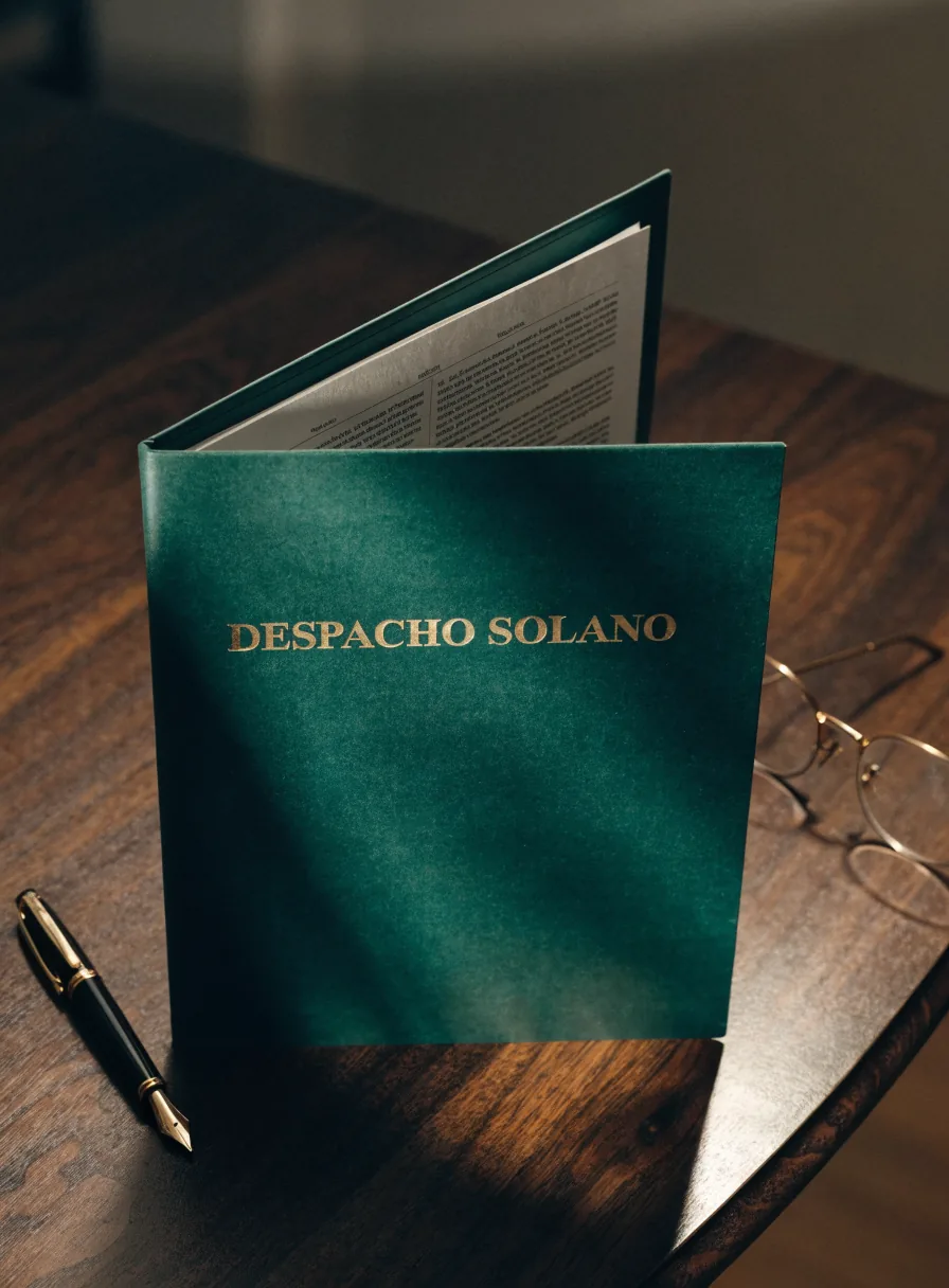 carpeta de expediente color verde oscuro con el nombre Despacho Solano en foil dorado, abierta con un contrato dentro, sobre un escritorio de nogal