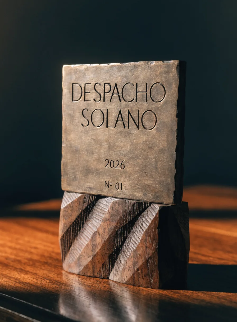 reconocimiento en bronce fundido grabado con Despacho Solano, el año 2026 y número 01, sobre una base de madera tallada a mano
