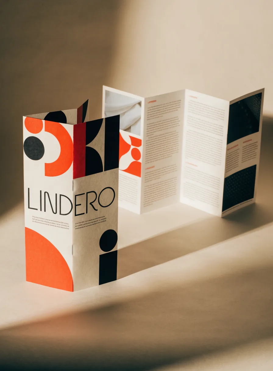Tríptico de identidad de la marca LINDERO desplegado de pie, con el logotipo, la paleta y los patrones geométricos en naranja, negro y crema