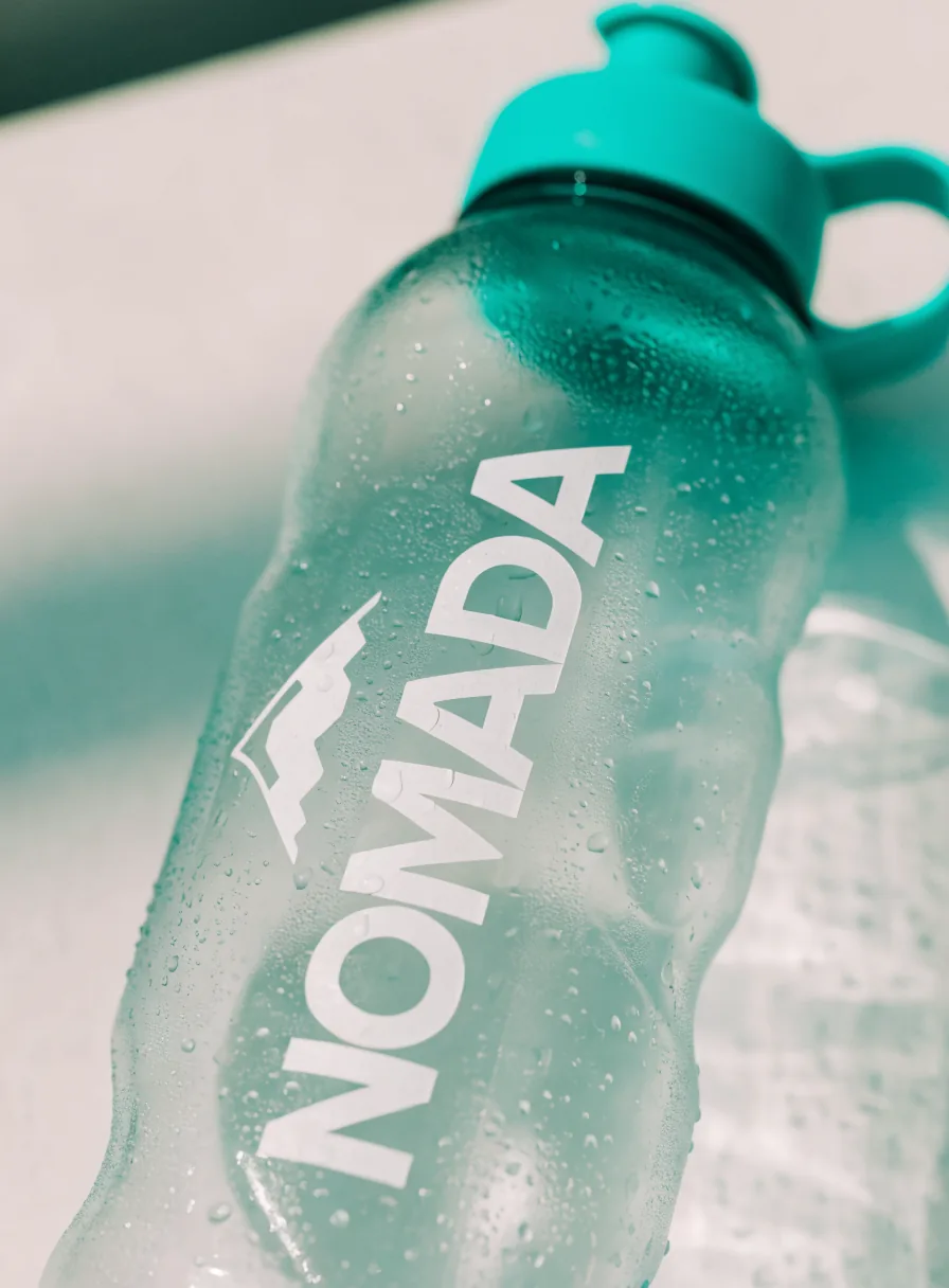 botella deportiva de tritán translúcido color turquesa con la marca ficticia Nómada impresa en blanco y gotas de agua