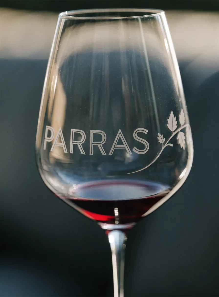 copa de vino de cristal con la marca ficticia PARRAS y una rama de vid grabadas al ácido, con vino tinto, sobre fondo oscuro