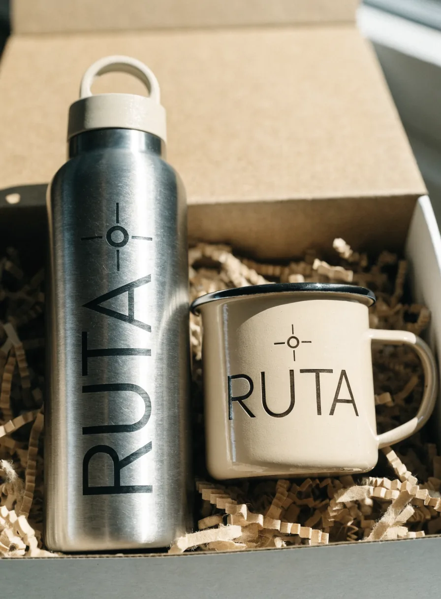 caja de regalo con relleno kraft, un termo de acero cepillado y una taza de peltre crema, ambos con la marca ficticia Ruta
