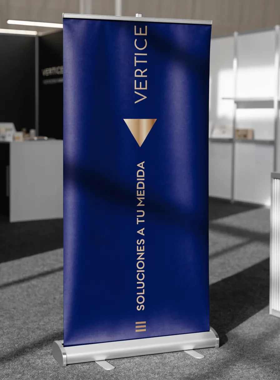 banner roll-up azul marino con la marca Vertice y la leyenda Soluciones a tu medida en dorado, montado en su base de aluminio en el pasillo de un pabellón