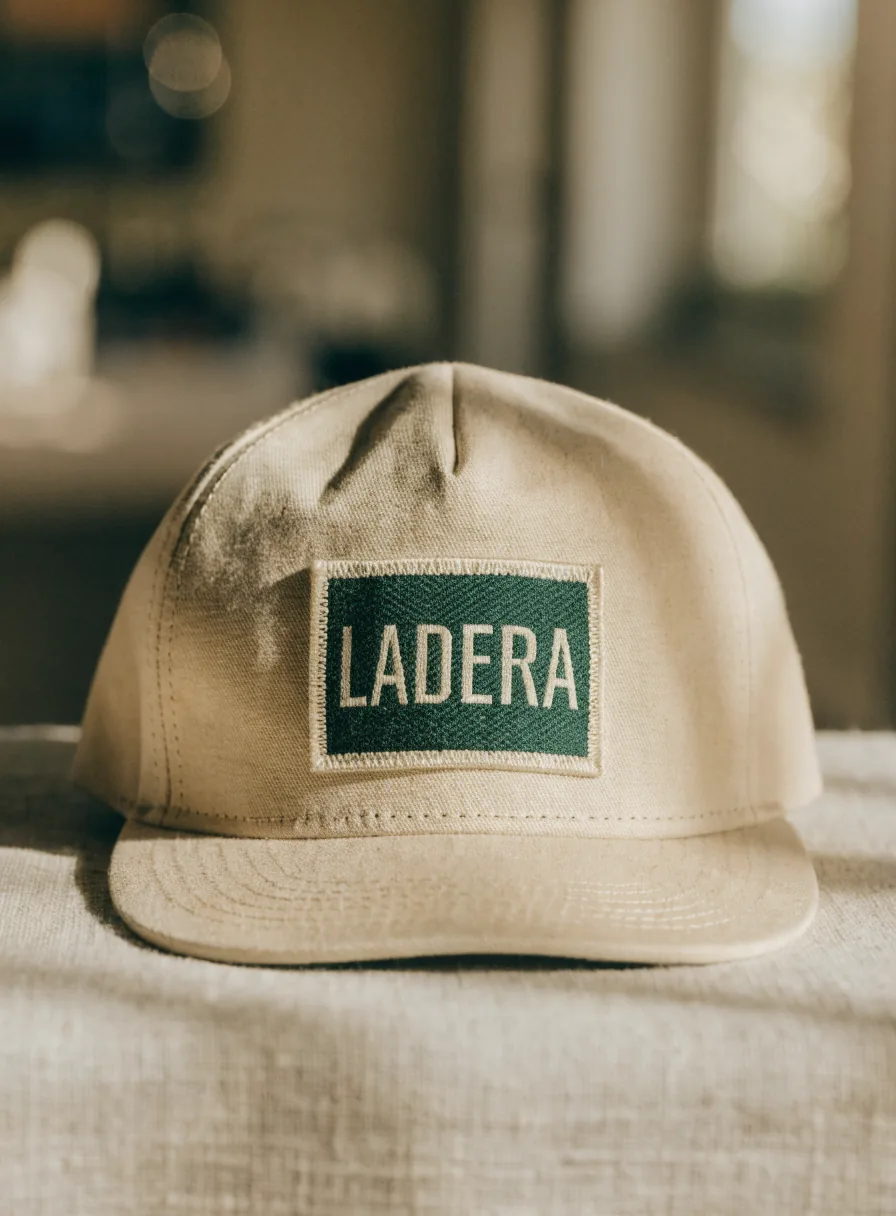 gorra estructurada de lona arena de pie sobre lino, con un parche jacquard tejido en verde bosque y crema cosido al frente con orilla merrow, que lleva tejida la marca ficticia LADERA