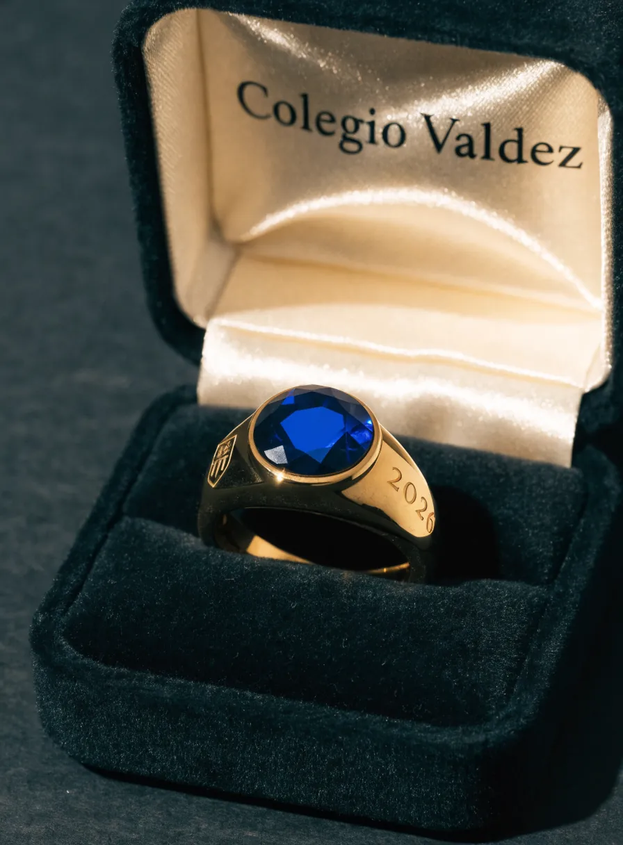 anillo de generación en oro con piedra azul facetada y el año 2026 grabado en el aro, en un estuche de terciopelo negro con el nombre del colegio