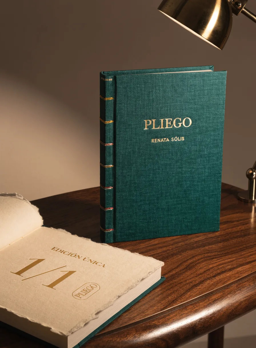 libro entelado en verde de la marca ficticia PLIEGO con el nombre en foil dorado y el lomo cosido a la vista, abierto junto a él un colofón numerado 1/1 sobre papel de algodón