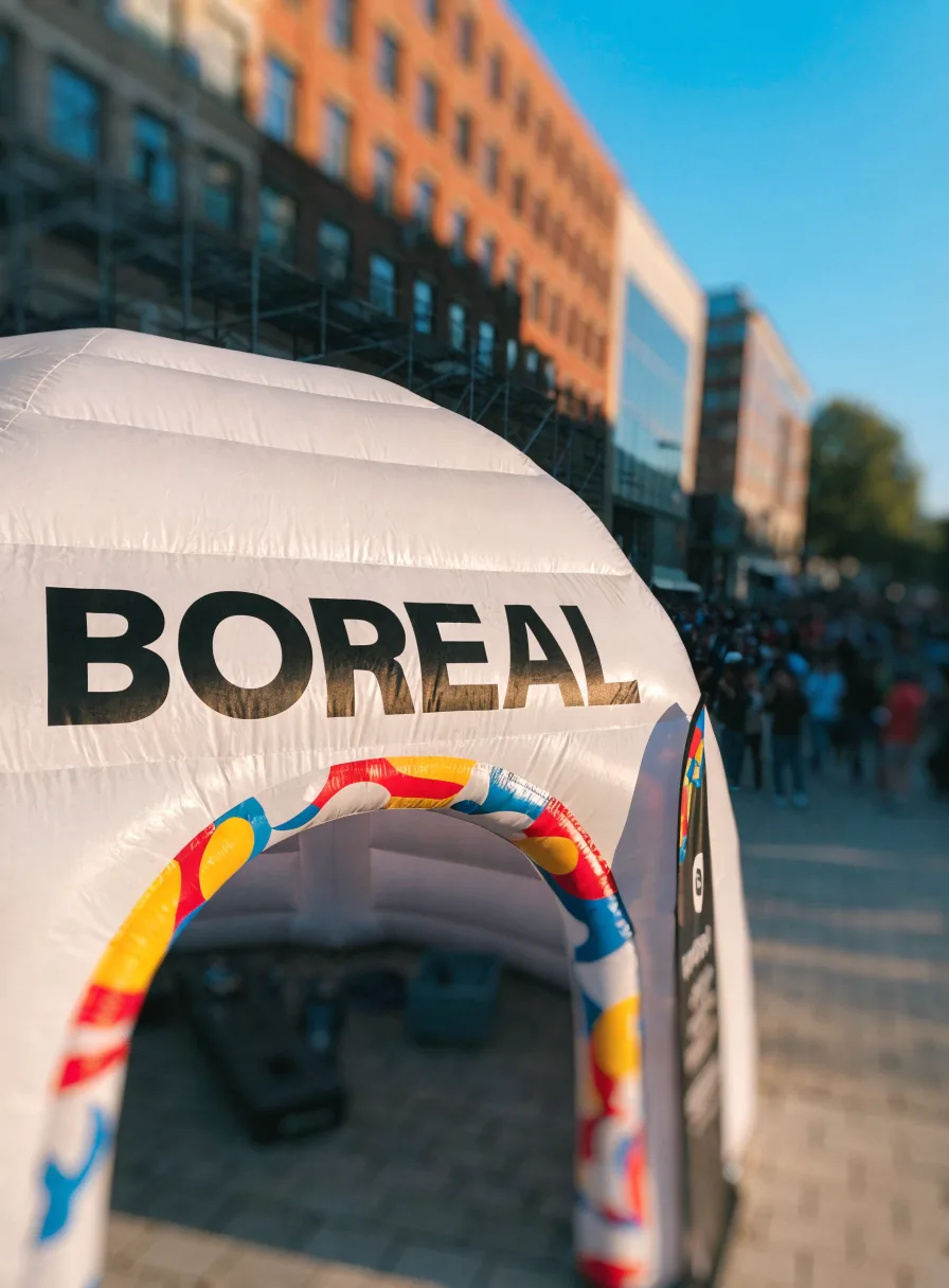 domo inflable blanco con tu marca en negro y un patrón de colores en el arco de entrada, en una activación de calle con gente al fondo