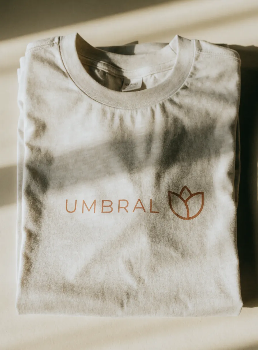 playera color arena doblada con la marca ficticia Umbral y un logo de tulipán estampados en terracota al centro del pecho