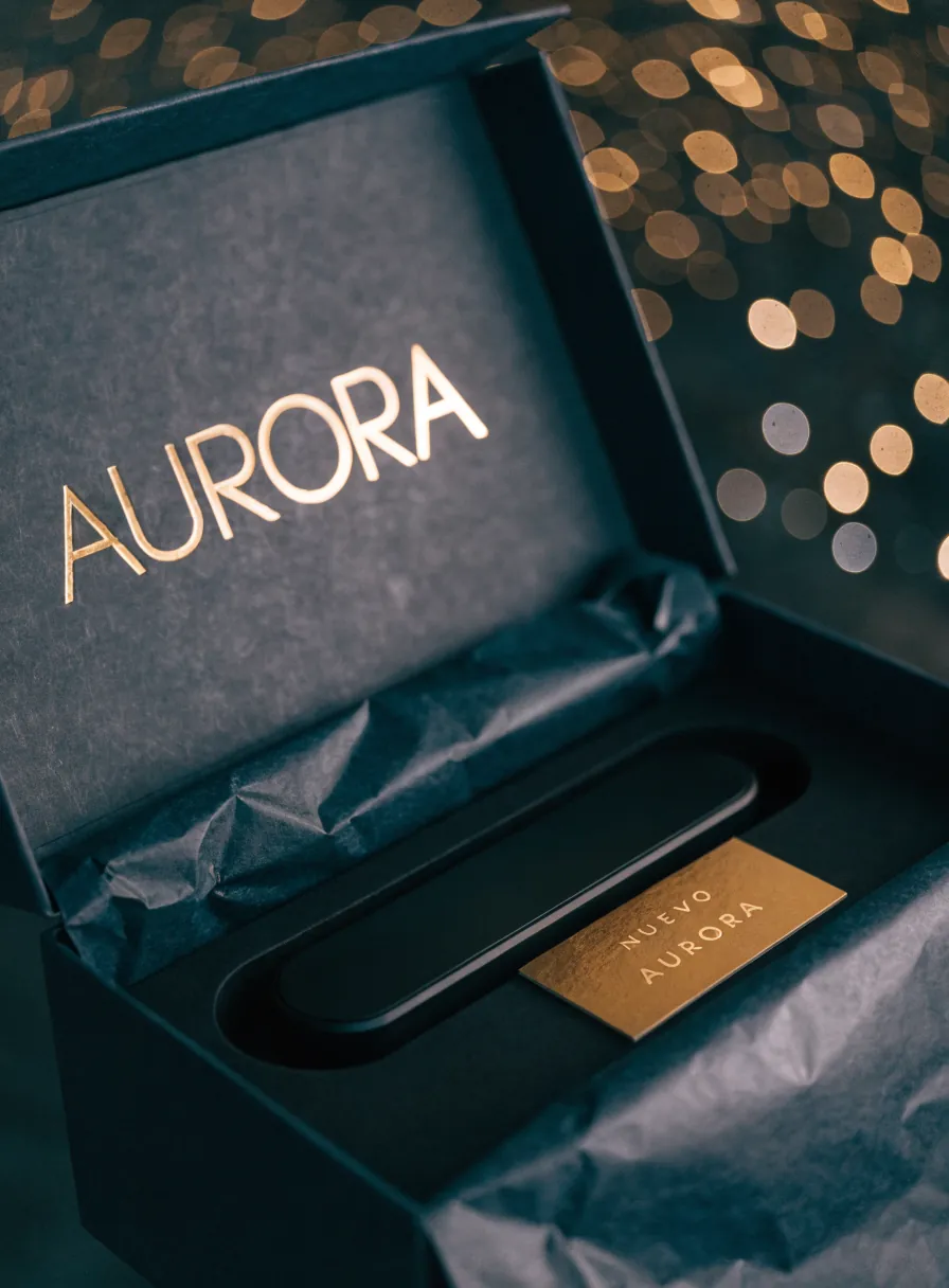 caja de reveal azul marino abierta con la marca Aurora en foil dorado dentro de la tapa, papel de seda y el producto anidado junto a una tarjeta Nuevo Aurora