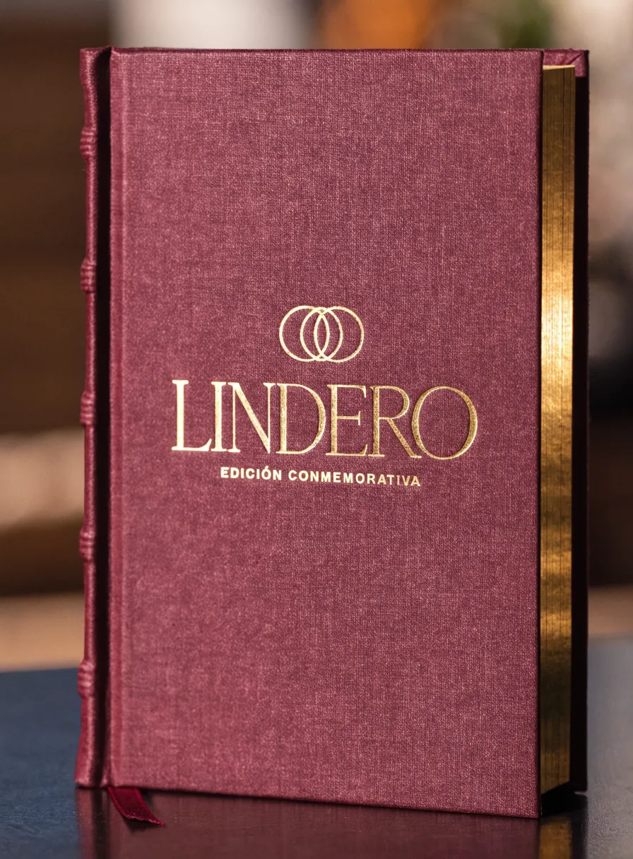 libro entelado en color vino de la marca ficticia LINDERO con edición conmemorativa en foil dorado, canto dorado, lomo de nervios y un listón separador