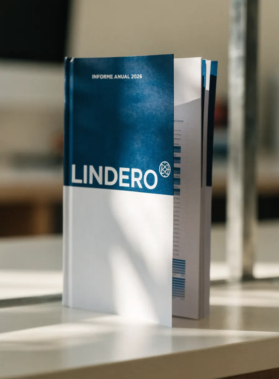informe anual de la marca ficticia LINDERO con la portada en azul y blanco que dice INFORME ANUAL 2026, de pie y abierto en páginas con gráficas y columnas de datos