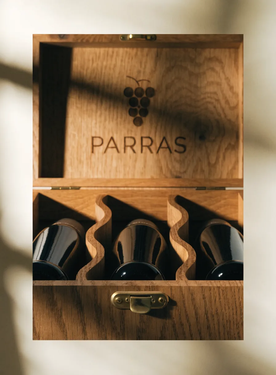 Caja cava de roble abierta con tres botellas de vino en un riel ondulado tallado y la tapa grabada con un racimo
