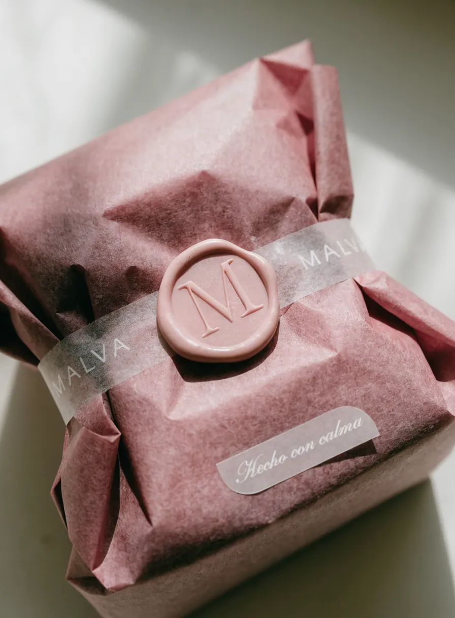 paquete envuelto en papel de seda rosa, cerrado con una faja de glassine MALVA y un sello de cera rosa con el monograma M en relieve