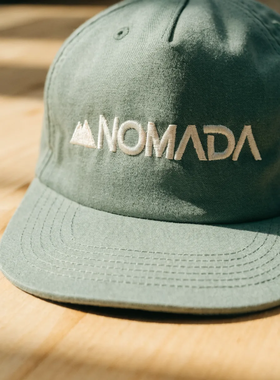 gorra de lona verde salvia con la marca ficticia Nómada bordada en hilo crema al frente