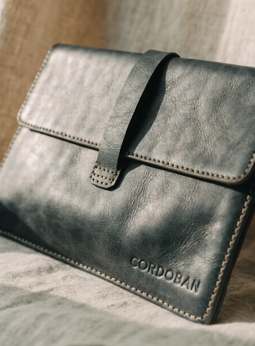 funda de piel gris azulada para laptop con cierre de correa y la marca ficticia CORDOBAN repujada, sobre lino
