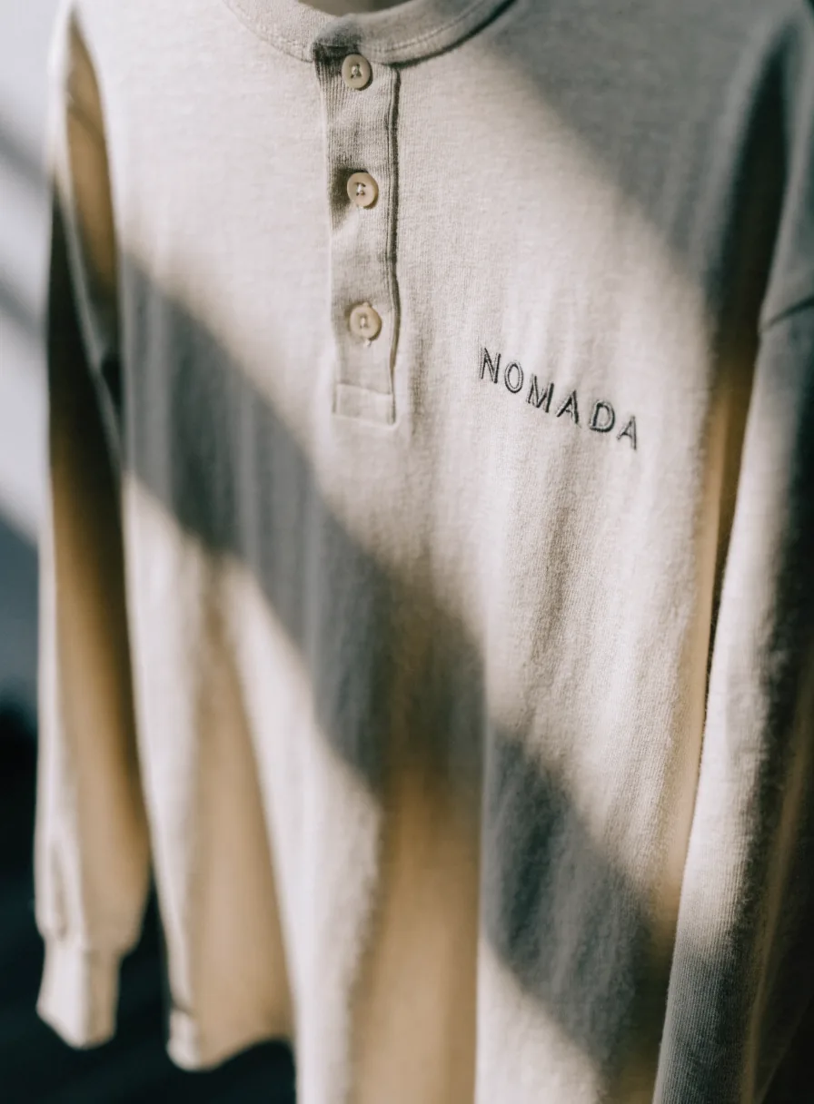 playera henley de manga larga color crema con placket de tres botones y la palabra NOMADA bordada tono sobre tono en el pecho