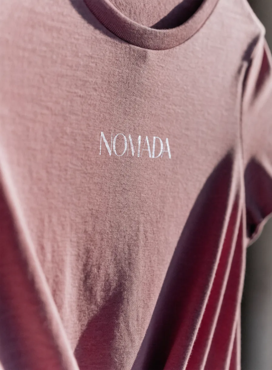 playera entallada de mujer en tono malva puesta sobre el cuerpo, con la palabra NOMADA impresa en letra fina blanca en el pecho