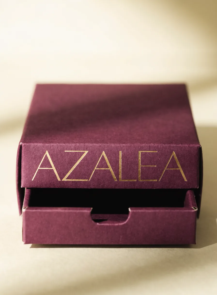 estuche tipo cajón deslizante en cartulina vino de la marca Azalea, con el nombre en foil oro sobre la funda y la charola entreabierta con muesca para el pulgar