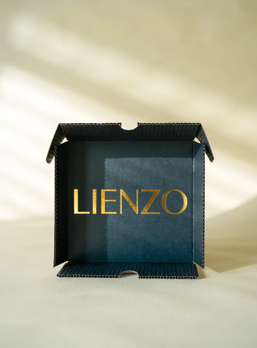 caja mailer de micro-corrugado teñido azul marino de la marca Lienzo, con las solapas abiertas que muestran la flauta del cartón y el nombre Lienzo en foil oro al centro