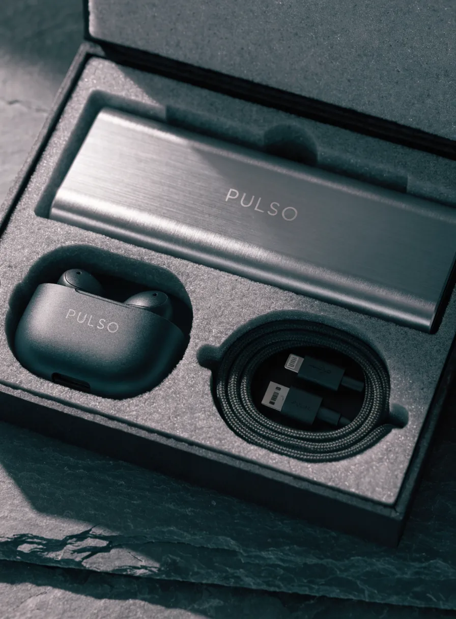 estuche gris pizarra abierto con una batería portátil Pulso, un estuche de audífonos Pulso y un cable trenzado, acomodados en espuma cortada a su medida
