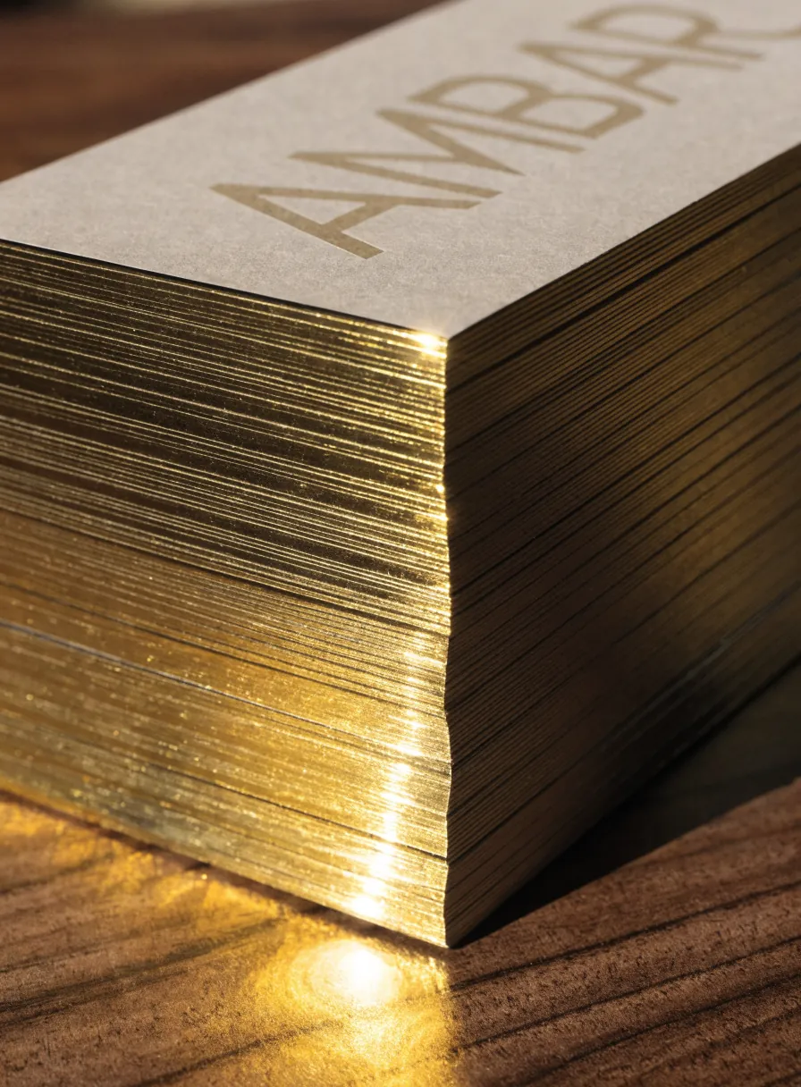 una pila de tarjetas de algodón de la marca ficticia ÁMBAR con el canto dorado metálico y el nombre en la cara superior