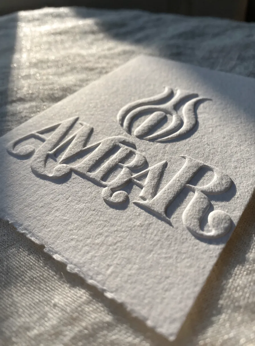 una tarjeta de papel de algodón de la marca ficticia ÁMBAR con el logotipo hundido en relieve seco profundo, sin tinta, sobre lino