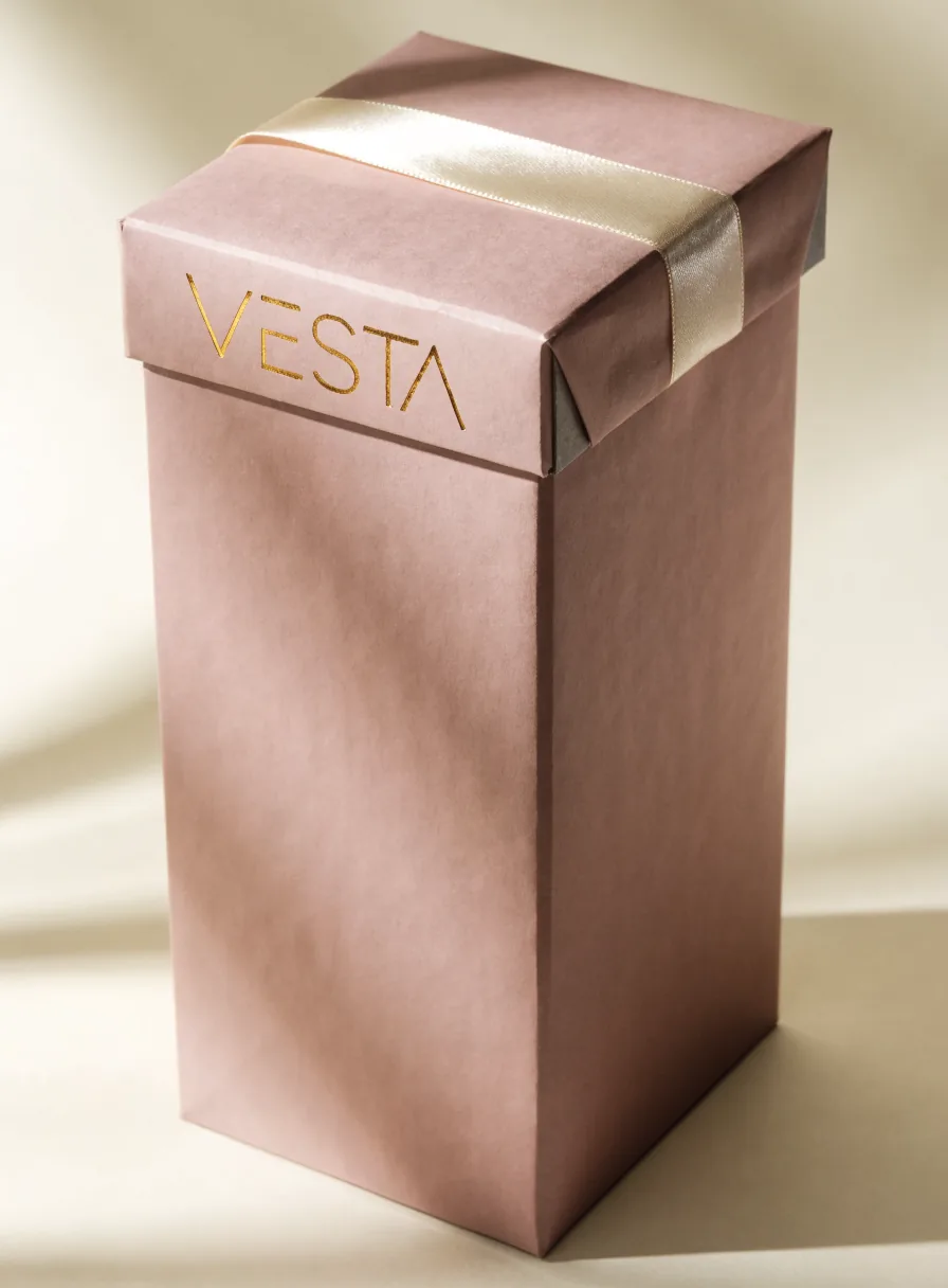 caja de regalo rígida en rosa palo con la palabra Vesta en foil oro sobre la tapa y un listón de raso color crema cruzándola