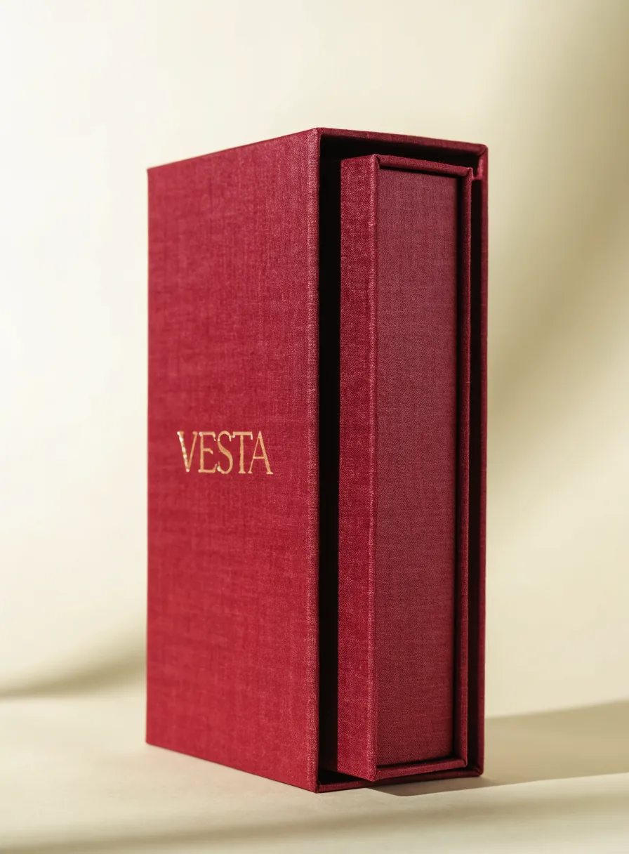 funda slipcase forrada en lino color vino con la palabra Vesta en foil oro, con el estuche interior deslizándose hacia afuera