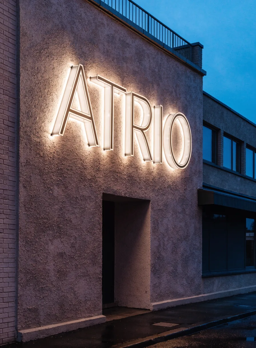 letras corpóreas iluminadas con halo de luz cálida y la marca ATRIO, montadas sobre la fachada de un local al anochecer