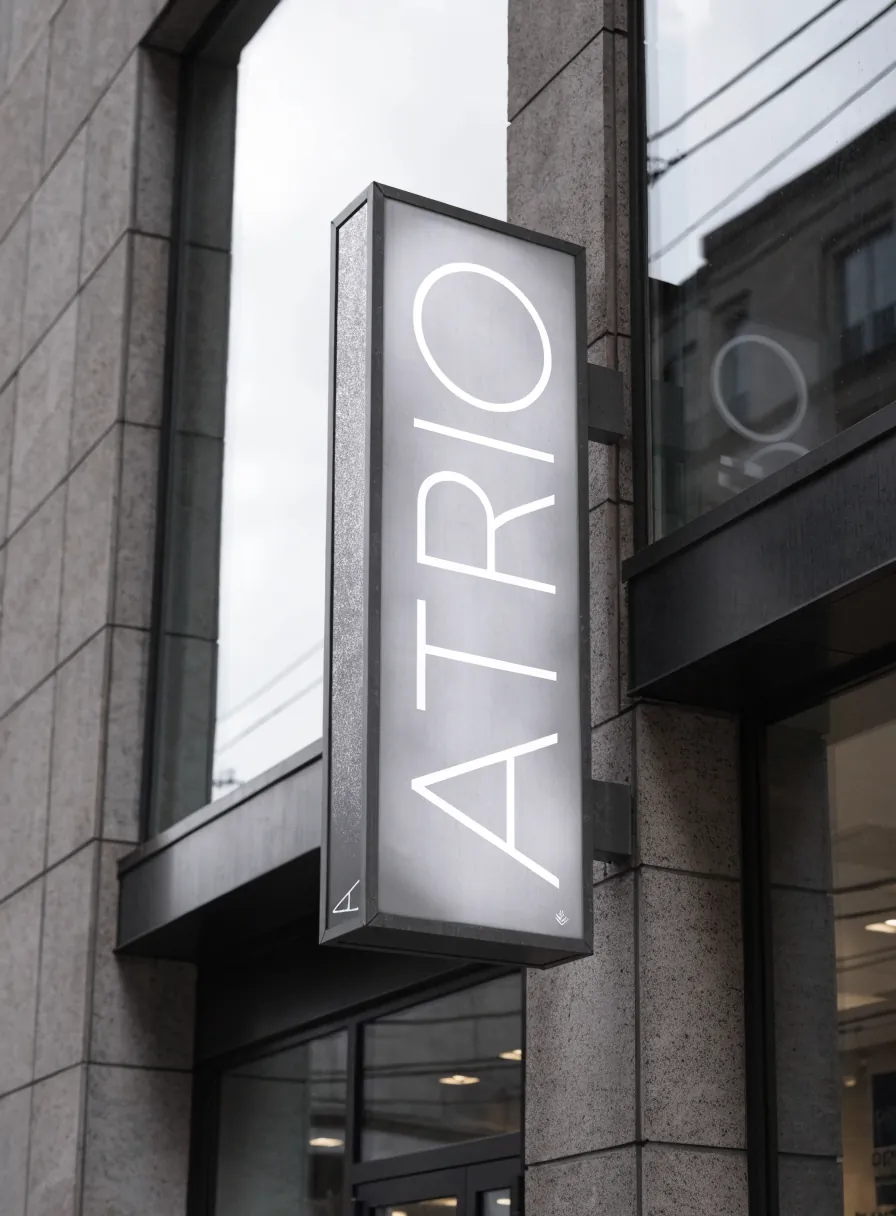 letrero luminoso tipo caja de luz con la marca ATRIO en vertical, saliente sobre la fachada de una tienda