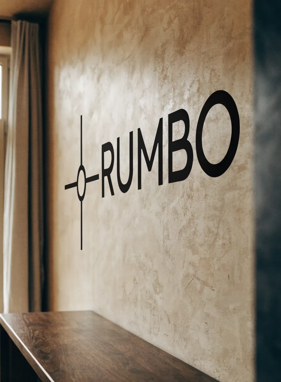 vinil decorativo de pared en negro con la palabra Rumbo y una rosa de los vientos, aplicado sobre un muro de pasta cálida junto a una barra de madera