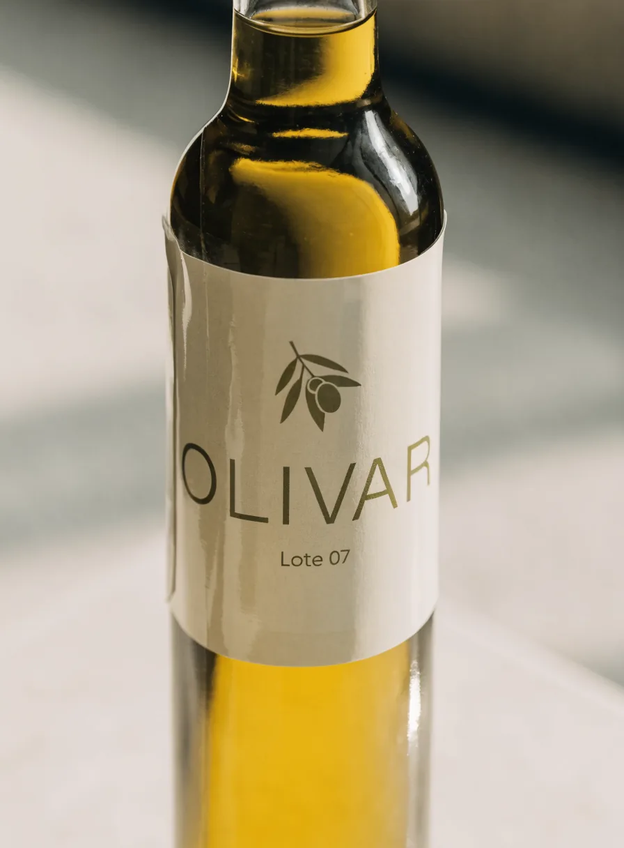 manga termoencogible mate color crema que envuelve el cuerpo de una botella de aceite de oliva Olivar, con una rama de olivo y el texto Lote 07, bajo luz lateral