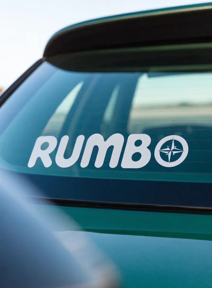 calcomanía de vinil de recorte en blanco con la marca Rumbo y una rosa de los vientos, aplicada sobre el medallón trasero de un auto color verde azulado